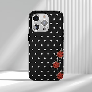 May include: Black phone case with a white polka dot pattern and three red ladybug illustrations. The case has a glossy finish and a black border, designed for a smartphone.