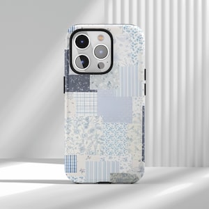 Op de afbeelding: Een telefoonhoesje met een patchwork-ontwerp in blauw- en wittinten. De hoes heeft een verscheidenheid aan patronen, waaronder bloemenprints, strepen en ruitjes, waardoor een unieke en gestructureerde uitstraling ontstaat. De hoes heeft een zwarte camerabehuizing.