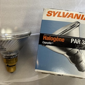 May include: A clear glass PAR38 halogen light bulb with a gold base, next to a box with the word SYLVANIA in orange letters. The box has the words "Halogène Capsylite PAR 38" on it.