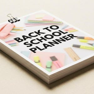 Puede incluir: Una pila de hojas de papel rectangulares con un clip de metal negro en la parte superior. La hoja superior presenta el texto negro en negrita BACK TO SCHOOL PLANNER sobre un fondo borroso de útiles escolares coloridos.