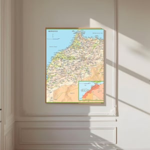 Op de afbeelding: Een ingelijste kaart van Marokko, met gedetailleerde geografische informatie. De kaart toont de grenzen, steden en geografische kenmerken van het land, met een kleinere inzetkaart. Het woord "MOROCCO" staat bovenaan gedrukt. De kaart zit in een houten lijst.