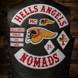 Op de afbeelding: Een zwart leren vest met witte en rode geborduurde patches. De achterkant toont de tekst HELLS ANGELS en NOMADS, samen met een gevleugeld schedelembleem, MC, 666, AFFA en ruitvormige 1%-patches. De zijkanten zijn geregen met zwarte leren veters.