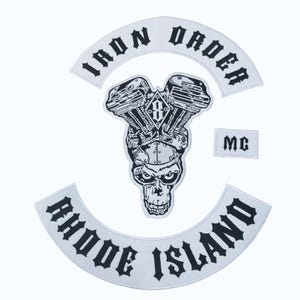 May include: A collection of white and black embroidered patches. The patches feature a skull with an engine, the words "IRON ORDER" and "RHODE ISLAND", and the letters "MC". These patches are likely for a motorcycle club.