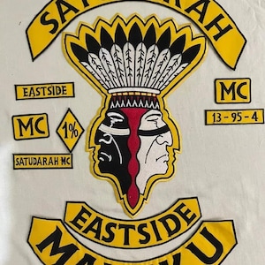 Op de afbeelding: Een verzameling geborduurde patches met gele en zwarte tekst en ontwerpen. De patches bevatten de woorden "SATUDARAH", "EASTSIDE" en "MALUKU". Een centrale patch toont twee gezichten, één zwart en één wit, met een gevederde hoofdtooi.