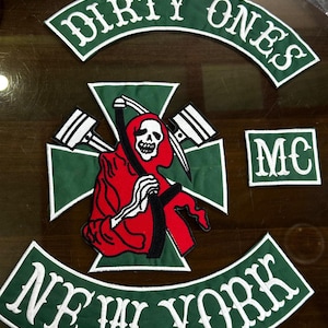 Op de afbeelding: Geborduurde patches in groen en wit. De patches tonen de woorden "DIRTY ONES" en "NEW YORK" in een gebogen ontwerp. Een centrale patch toont een rode zeisfiguur met een zeis en de letters "MC".