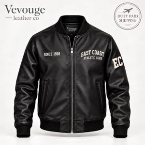Pode incluir: Um blusão bomber de couro preto com gola, punhos e bainha canelados. A frente apresenta um fecho de correr prateado, dois bolsos laterais e texto branco "SINCE 1988" e "EAST COAST ATHLETIC CLUB", com "EC" impresso na manga esquerda.