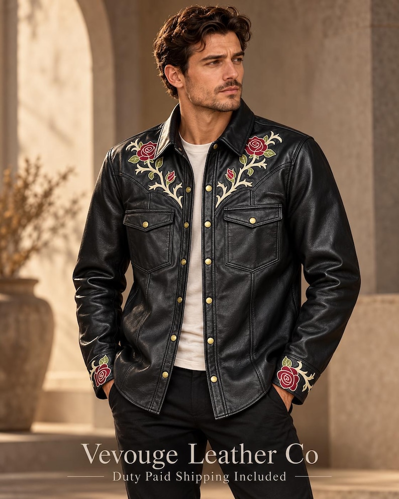 May include: A black leather shirt jacket featuring embroidered red rose motifs with green leaves on the chest and cuffs. The garment includes a pointed collar, two chest pockets with flaps, and gold-toned metal snap buttons down the front.
