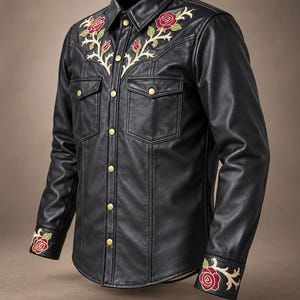 May include: A black leather shirt featuring gold-tone snap buttons, two chest pockets, and floral embroidery with red roses and cream-colored vines on the collar yoke and cuffs. The text Vevouge Leather Co is printed at the bottom.