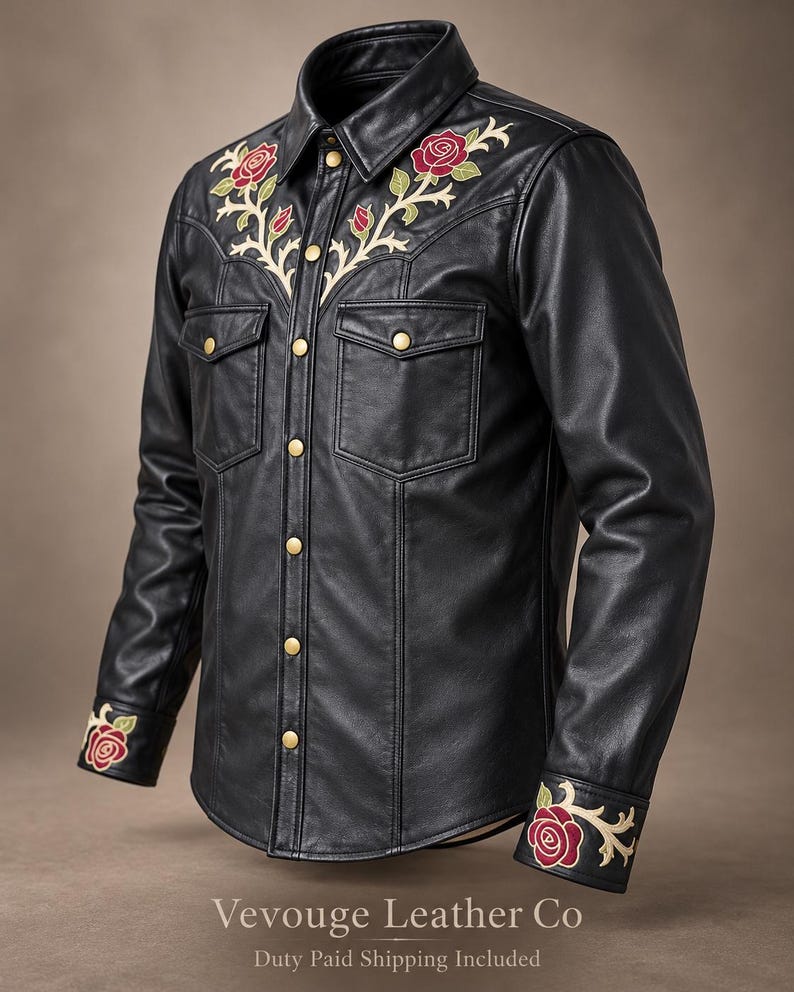 May include: A black leather shirt featuring gold-tone snap buttons, two chest pockets, and floral embroidery with red roses and cream-colored vines on the collar yoke and cuffs. The text Vevouge Leather Co is printed at the bottom.