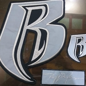 Puede incluir: Conjunto de parches bordados con la letra "B" estilizada en gris, negro y plateado. Incluye un parche grande, otro más pequeño y un parche rectangular con texto escrito.