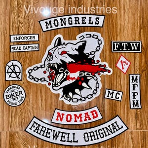 Peut inclure: Un ensemble d'écussons brodés présentant un motif central de tête de loup avec des accents rouges et des chaînes, entouré d'écussons textuels dont MONGRELS, NOMAD, FAREWELL ORIGINAL, ENFORCER, ROAD CAPTAIN, F.T.W, MC, MFPM et un écusson losange 1%.