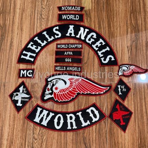 Könnte beinhalten: Eine Sammlung bestickter Aufnäher mit den Schriftzügen HELLS ANGELS, NOMADS, WORLD, WORLD CHAPTER, AFFA, 666 und MC. Das Set enthält ein großes geflügeltes Totenkopf-Emblem, zwei rautenförmige 1%-Aufnäher und geschwungene Rocker-Aufnäher mit roten Rändern.