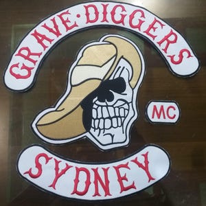 May include: Embroidered patch set featuring a skull wearing a cowboy hat. The top patch reads "GRAVE DIGGERS" in red letters on a white background. The bottom patch says "SYDNEY". A small patch reads "MC".