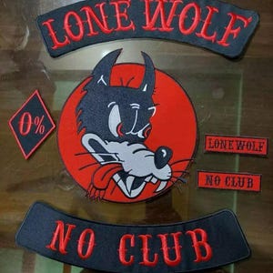 May include: A collection of black and red embroidered patches. The central patch displays a cartoon wolf's head on a red background. The words "LONE WOLF" and "NO CLUB" are arched above and below. A small diamond patch reads "0%".