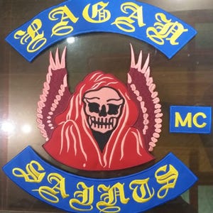 May include: Embroidered patch set featuring a central grim reaper design in red and black, with a skull face. The patch set includes arched blue patches with yellow lettering that reads "RAGAN" and "SAINTS", and a small rectangular patch with "MC".