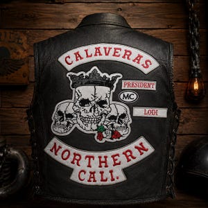 Puede incluir: Chaleco de cuero negro con parches. Los parches incluyen las palabras "CALAVERAS" y "NORTHERN CALI." en letras rojas y blancas. El chaleco también presenta gráficos de calaveras y la palabra "LODI."
