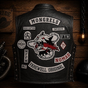 Op de afbeelding: Een zwart leren motorvest met diverse geborduurde patches, waaronder een centrale afbeelding van een grommende hondenkop met een ketting, en de teksten MONGRELS, ROAD CAPTAIN, ENFORCER, F.T.W, 1%, NOMAD, MFFM, MC en FAREWELL ORIGINAL.