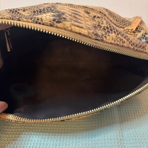 Peut inclure: Un sac &agrave; main &agrave; motif peau de serpent avec une fermeture &eacute;clair dor&eacute;e. L'int&eacute;rieur est marron fonc&eacute;. Le sac est ouvert, r&eacute;v&eacute;lant l'int&eacute;rieur. Le motif peau de serpent pr&eacute;sente des nuances de marron, de beige et de noir.