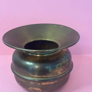 Peut inclure: Un vase vintage en laiton avec un bord évasé et un corps arrondi. Le vase présente une patine sombre et vieillie avec des zones de laiton apparentes, suggérant son âge. Le design est simple et élégant, adapté pour exposer de petites fleurs ou des objets décoratifs.