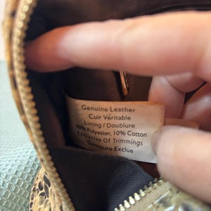 Peut inclure: Gros plan sur un petit sac &agrave; main &agrave; motifs avec une fermeture &eacute;clair. L'int&eacute;rieur du sac est visible, ainsi qu'une &eacute;tiquette indiquant "Genuine Leather, Cuir V&eacute;ritable, Lining/Doublure, 90% Polyester, 10% Cotton, Exclusive Of Trimmings, Garniture Exclue."