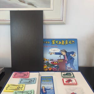Peut inclure: Jeu de société "VENTES en folie" avec des illustrations colorées et du texte. Le jeu comprend de l'argent factice, des pions et des dés. La boîte présente un dessin animé d'un homme à un podium avec des voitures en arrière-plan.