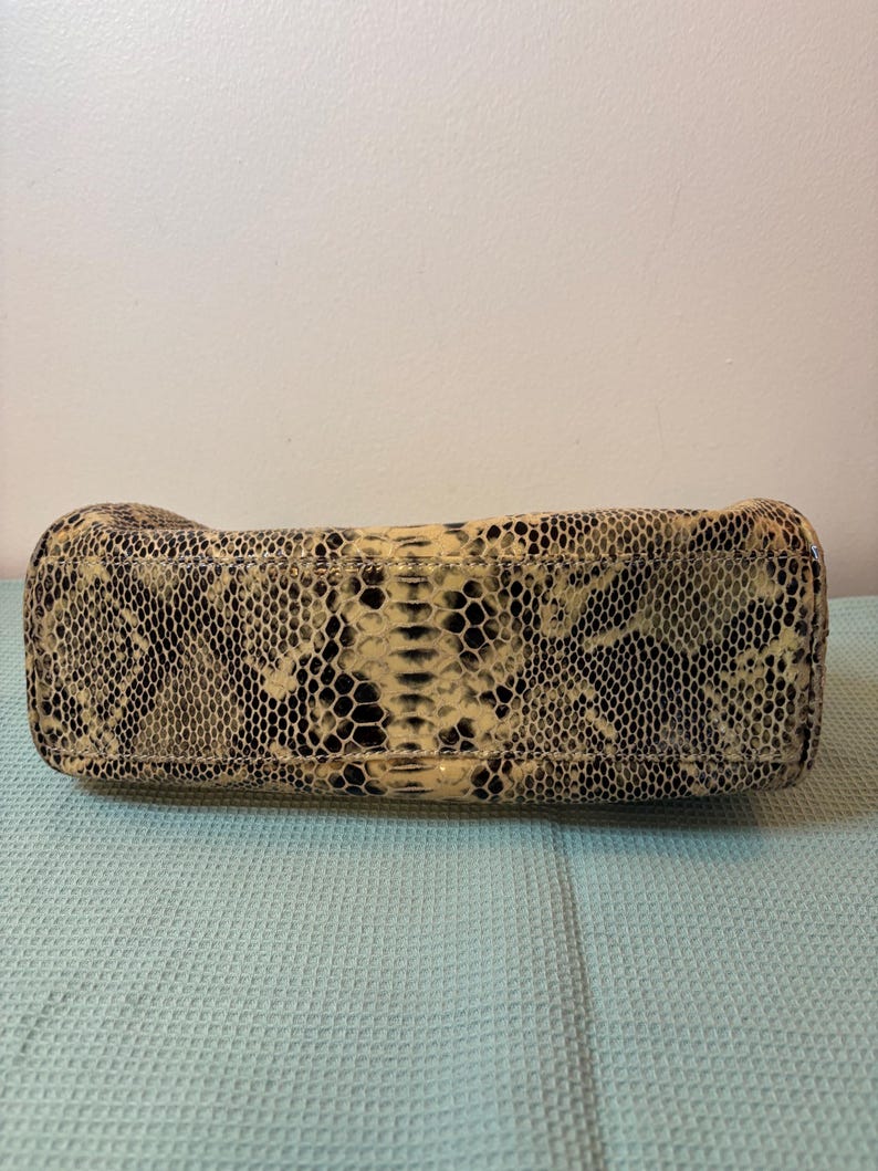 Peut inclure: Un sac &agrave; main rectangulaire avec un motif peau de serpent dans les tons beige, noir et cr&egrave;me. Le design du sac imite la texture et la coloration des &eacute;cailles de serpent, offrant un accessoire unique et &eacute;l&eacute;gant.
