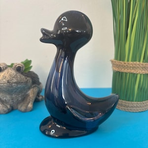 Peut inclure: Une figurine de canard en céramique bleu foncé brillant. Le canard a un long cou et un corps arrondi, avec un petit bec et une surface lisse et réfléchissante. L'objet est décoratif.