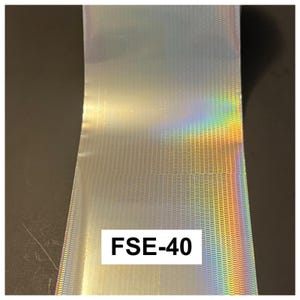 May include: A roll of silver holographic foil featuring a repeating pattern of small, horizontal, wave-like indentations. The surface reflects a spectrum of rainbow colors when light hits it. A white rectangular label displays the text FSE-40.