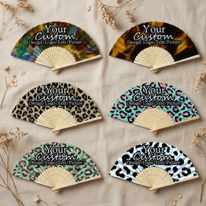 Op de afbeelding: Zes openstaande handwaaiers met houten handvatten. De waaierbladen tonen verschillende ontwerpen, waaronder dierenprints en abstracte patronen. Op elke waaier staat de tekst "Your Custom Design/Logo/Text/Picture".
