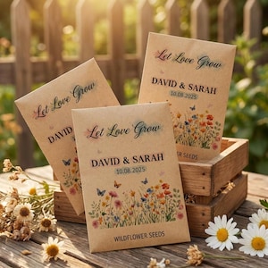 以下が含まれることがあります： 「Let Love Grow」の文字と名前、日付が書かれた茶色の紙の種子袋が3つ。カラフルな花と蝶で飾られています。木製の箱に入っており、木製のテーブルの上に置かれています。