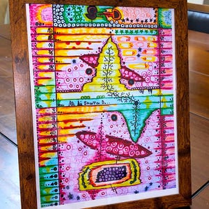 May include: Abstract art print in a wooden frame. The artwork features a colorful, patterned design with pink, yellow, green, and blue hues. The print includes the text "MiStara D..." and various symbols and shapes.