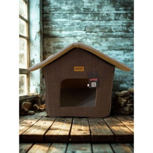 May include: A brown pet house with a house-shaped design. The pet house has a tan roof and a rectangular opening. The brand name "LEPUS" is visible on a tag attached to the house. The house is made of a textured fabric.