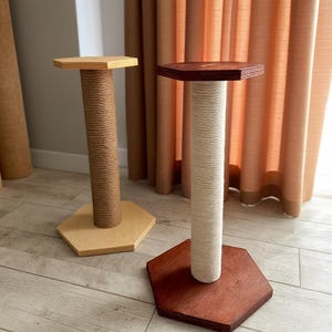 Puede incluir: Dos rascadores para gatos. Uno tiene una base y parte superior de madera marrón claro con un centro envuelto en cuerda de sisal. El otro tiene una base y parte superior de madera marrón oscuro con un centro envuelto en cuerda color crema. Ambos postes son hexagonales.