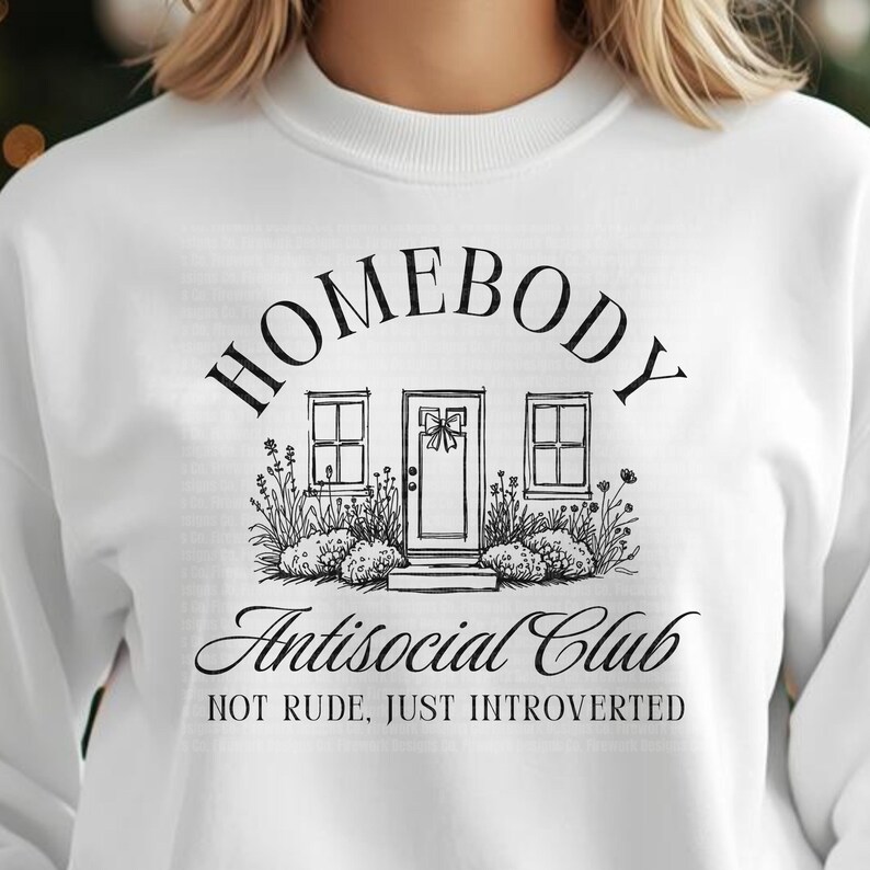 May include: White sweatshirt featuring a black graphic. The design includes the word "HOMEBODY" above a house illustration, with "Antisocial Club" below. The text "NOT RUDE, JUST INTROVERTED" is printed beneath.