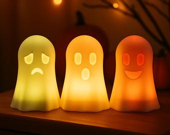 Op de afbeelding: Drie spookvormige nachtlampjes met verschillende gezichtsuitdrukkingen. De lampen zijn geel, oranje en rood, wat een warme sfeer creëert. Perfect voor Halloween of thema-decoratie.