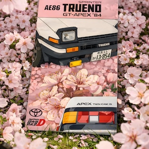 Puede incluir: Un póster rosa con una ilustración de un coche AE86 Trueno GT-Apex '84 blanco y negro con flores de cerezo. El póster incluye el texto "SPRINTER AE86 TRUENO GT-APEX '84" e "INITIAL D".