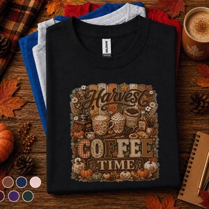 May include: A black t-shirt featuring a graphic print with the text Harvest Coffee Time. The design includes illustrations of coffee mugs, a coffee grinder, a bag of coffee beans, maple syrup, and various pumpkins surrounded by autumn leaves and flowers.