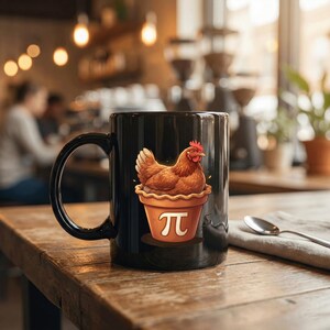 May include: Black ceramic coffee mug featuring a brown hen illustration inside a pie-shaped container with the pi symbol. The mug has a large handle and is set on a wooden surface. The background is blurred, suggesting a cafe setting.
