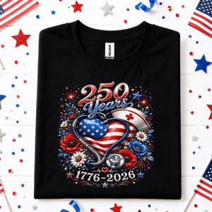 May include: Black t-shirt with a patriotic design celebrating 250 years. The graphic includes a heart with the American flag, a nurse's cap, and the years 1776-2026. Red, white, and blue stars and flowers surround the central design.