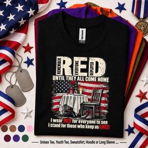 Puede incluir: Una camiseta negra con un gráfico de una mesa con mantel blanco, una rosa roja y una vela frente a una bandera estadounidense. El texto dice: REMEMBER EVERYONE DEPLOYED UNTIL THEY ALL COME HOME y I wear RED to see I stand for those who keep us FREE!
