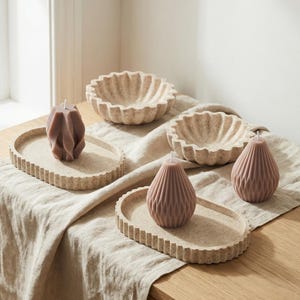 Puede incluir: Una colección de velas y bandejas decorativas en tonos neutros. La imagen presenta dos bandejas ovaladas con bordes texturizados, cada una con una vela. También hay dos cuencos redondos y acanalados y dos velas adicionales.