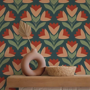 May include: A decorative scene featuring a teal floral wallpaper with red and peach-colored tulip-like flowers. A round, peach-colored vase with a hole in the middle and a woven basket sit on a wooden shelf against a white brick wall.