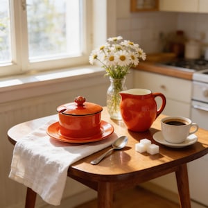 May include: A still life featuring a small wooden table with a red ceramic sugar bowl and creamer, a cup of coffee, and a vase of daisies. A white linen napkin and a spoon are also on the table.
