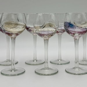 May include: Set of seven clear wine glasses with a decorative swirl design in the bowl. The glasses have long stems and round bases. The swirl design features shades of purple, gold, and blue.