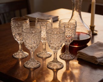 May include: A set of five clear glass goblets featuring a geometric diamond-cut pattern on the bowl and a short, sturdy stem. The glasses are arranged in a cluster, each with a circular base and a textured surface that catches the light.
