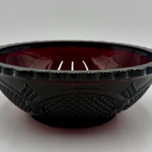 May include: A ruby-red glass bowl with a decorative, textured exterior. The bowl has a scalloped rim and diamond-patterned sides. The interior of the bowl is a deep red color. This vintage bowl is a decorative piece.