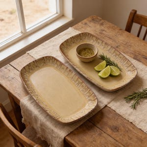 May include: Two rectangular ceramic serving platters with a light beige finish and a dark brown etched geometric pattern along the rim. One platter holds a small round bowl filled with green sauce, three lime wedges, and a sprig of fresh rosemary.
