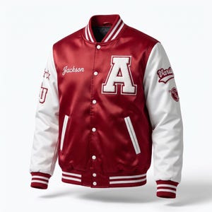 May include: A maroon satin varsity jacket with white sleeves, featuring a large white letter A on the chest, the name Jackson embroidered in white, and various white patches on the sleeves including the text Varsity and the letters JU.