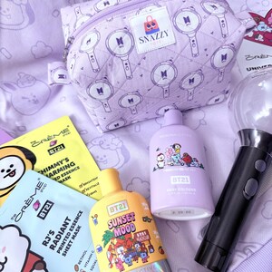 May include: A collection of BT21-themed beauty products and accessories. Includes a lavender quilted cosmetic bag with a zipper, sheet masks, and body cologne bottles. The bag features a repeating pattern of a microphone design. The products are in shades of yellow, purple, and black.