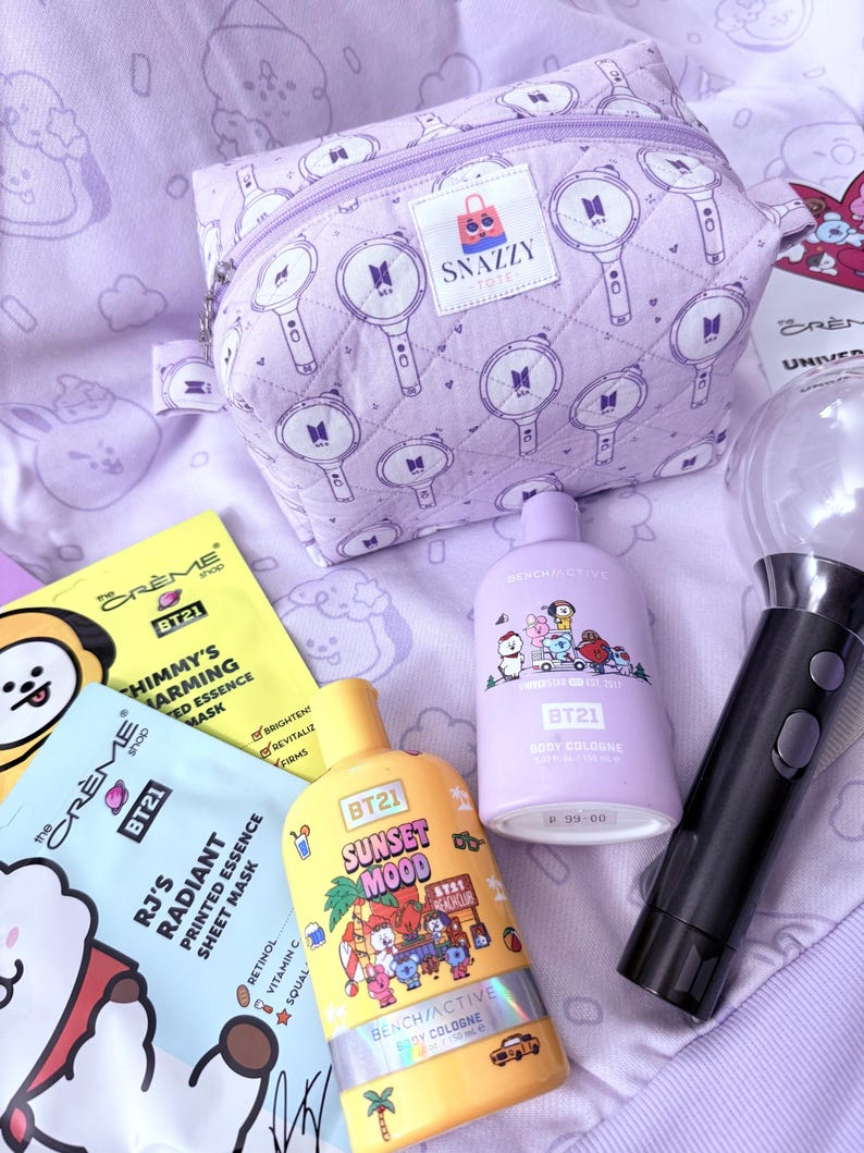 May include: A collection of BT21-themed beauty products and accessories. Includes a lavender quilted cosmetic bag with a zipper, sheet masks, and body cologne bottles. The bag features a repeating pattern of a microphone design. The products are in shades of yellow, purple, and black.